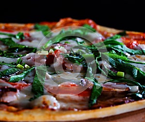 Italian hot pizza with tomato, spinach and pieces of bÐ°Ñon isolated on black background